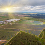 An aerial view of a solar power plant in a vast open field, with the sun shining on a cloudy sky.