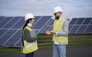 A man and woman in vests talking on a solar farm